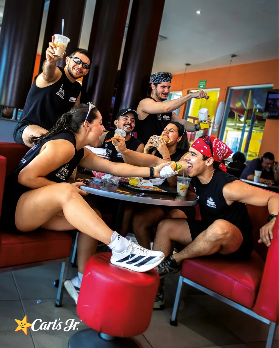 El grupo ocupa una mesa del restaurante: unos sentados en el sillón, otro recostado en el suelo con los tenis en alto, todos con vasos en la mano.