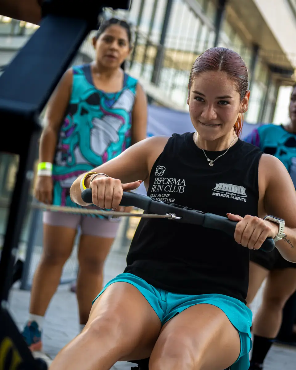 Una corredora del club, con la playera negra de Reforma Run Club, tira de una máquina de remo durante el circuito; detrás, otras dos esperan su turno.